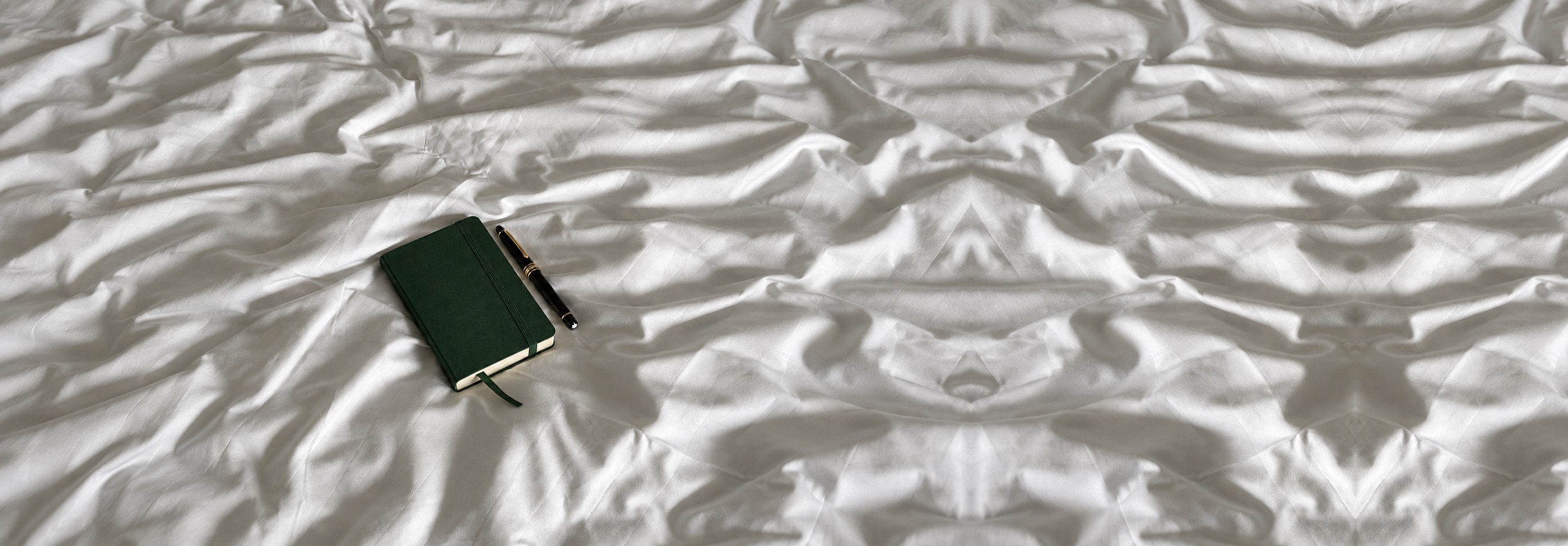 A green notebook and fountain pen resting on white linen