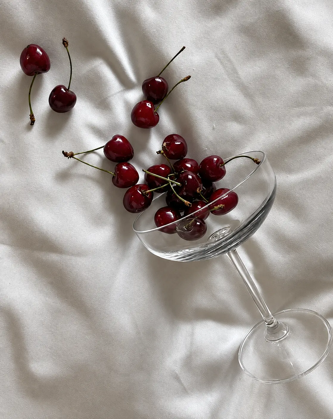 Dark cherries spilling from a coupe glass onto pale silk